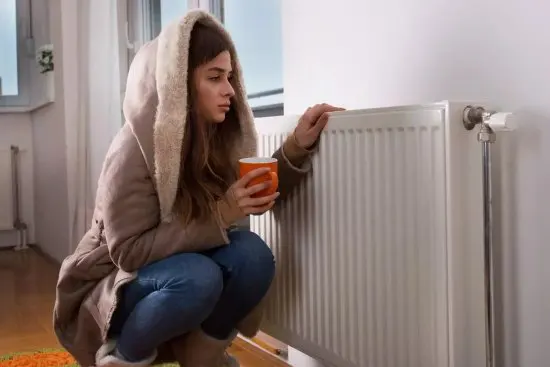 Une fille en manteau appuyée contre un radiateur à cause d'une chaudière encrassée par le calcaire.